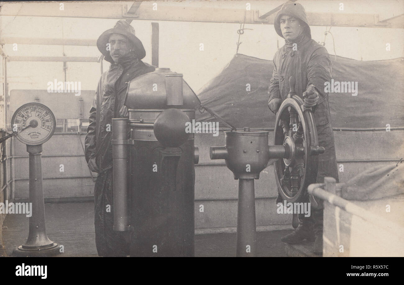 * Maritime Vintage Carte postale photographique de deux hommes portant des vêtements pour temps humide sur le pont d'un bateau. L'un des hommes de la Direction de la roue du navire. Banque D'Images