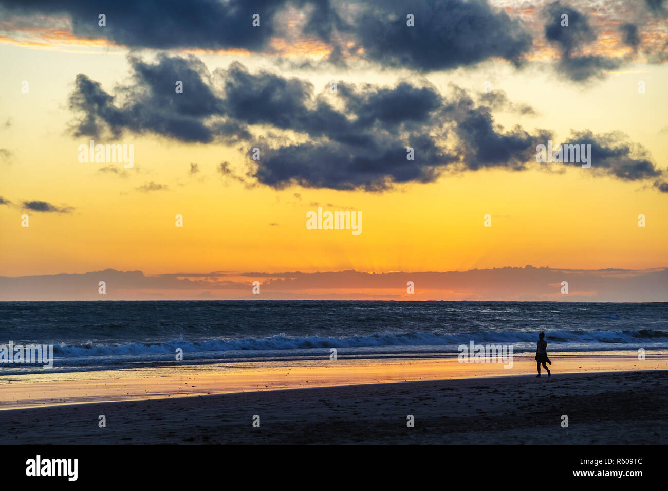 Jeune femme marche le long de la plage au coucher du soleil Banque D'Images