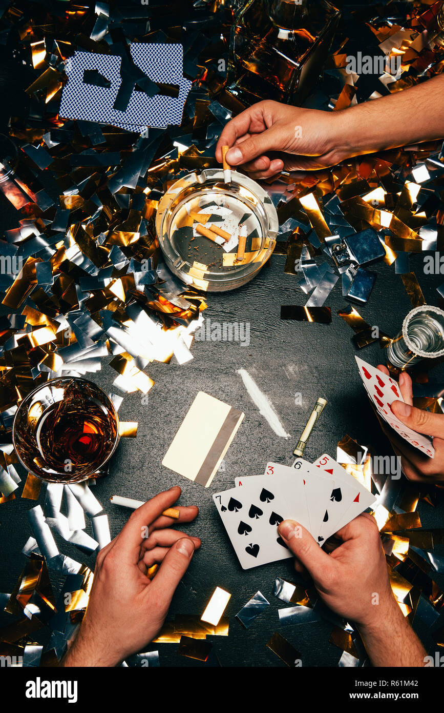 Vue partielle des hommes jouant au poker avec la cocaïne, l'alcool et les cigarettes à table couverte par golden confetti Banque D'Images