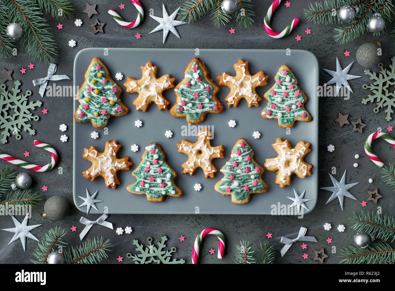 Assiette de cookies de Noël en forme d'arbres de Noël et des flocons sur plaque gris. Télévision lay, fond sombre décoré de branches de sapins, des cannes de bonbon, st Banque D'Images