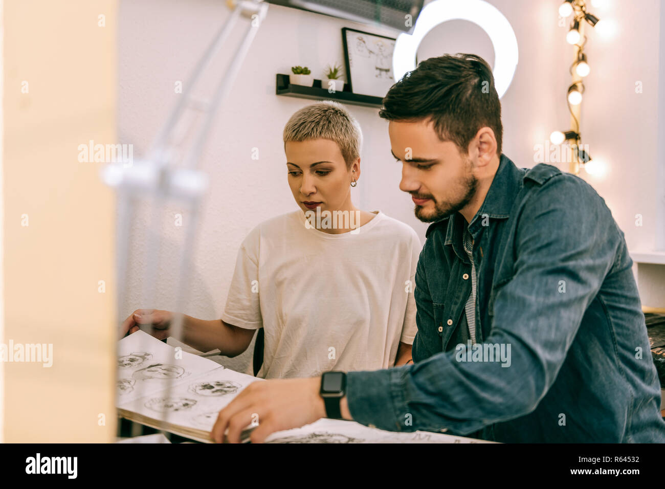 Beau barbu en veste jeans client assis avec maître tatouage Banque D'Images