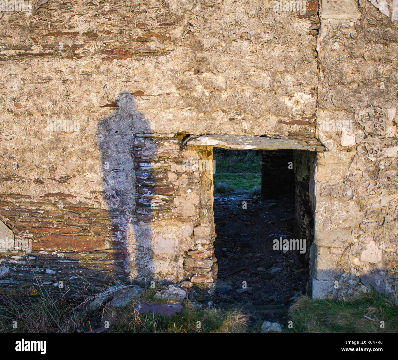Ombre sinistre à côté d'une porte de pierre sur un mur en pierre au lever du soleil. Banque D'Images