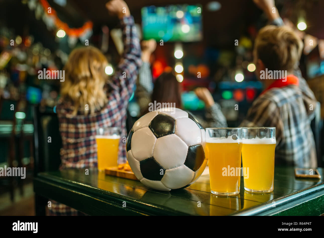 Ball et de la bière sur la table dans un bar sportif, les fans de football sur l'arrière-plan. La diffusion TV, regarder le jeu concept Banque D'Images