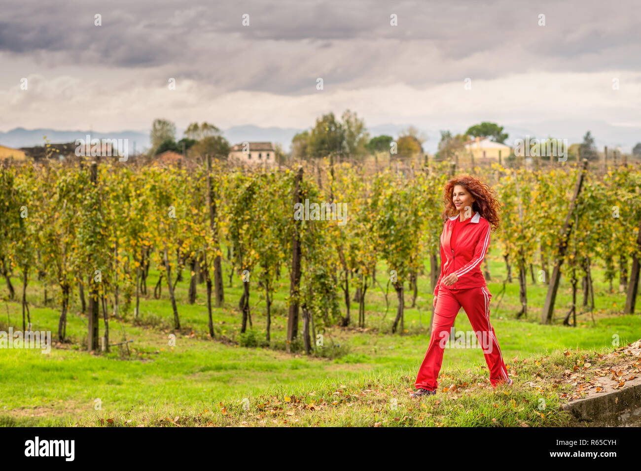 Girl in red sport suit smiling et marcher le long de vignes vertes. de long cheveux rouges et caractéristiques du Moyen-Orient Banque D'Images