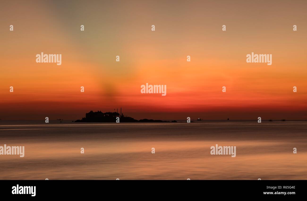 Un orange-feu lever du soleil ciel surplombant la mer de Chine du sud dans la baie de Nha Trang au Vietnam. Avec les bateaux de pêche et une petite île de silhouette. Banque D'Images