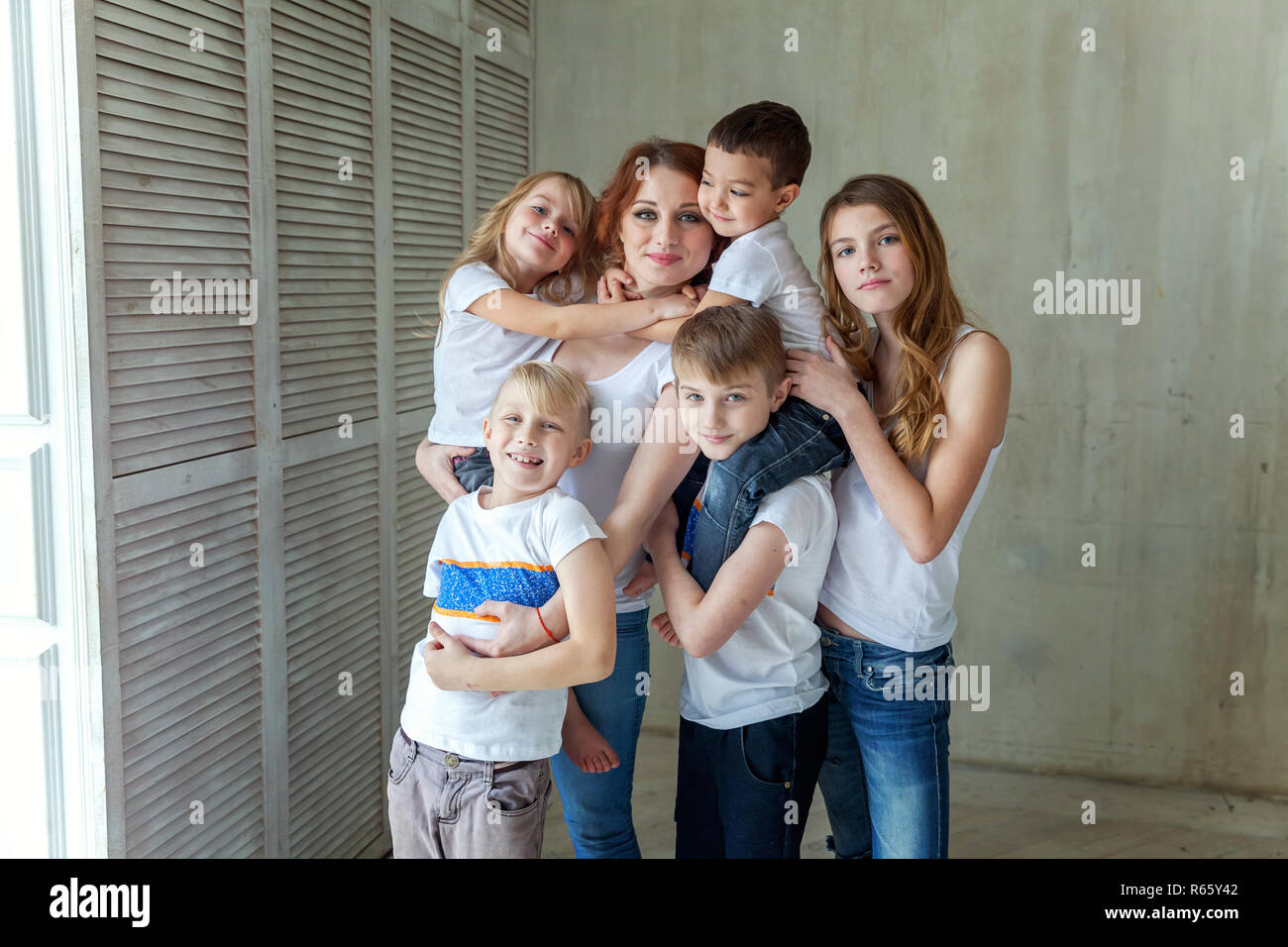 Famille heureuse mère et cinq enfants près du mur à la maison. Femme et les petits enfants se détendre dans une chambre blanche. Famille heureuse à la maison. Jeune mère jouant w Banque D'Images