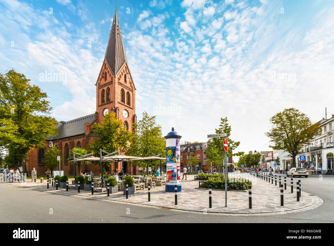 La tour de l'église de Warnemunde néogothique s'élève au-dessus de la ville côtière de Rostock, Allemagne, en tant que touristes et les Allemands dîner sur le patio dans le carré ouvert. Banque D'Images