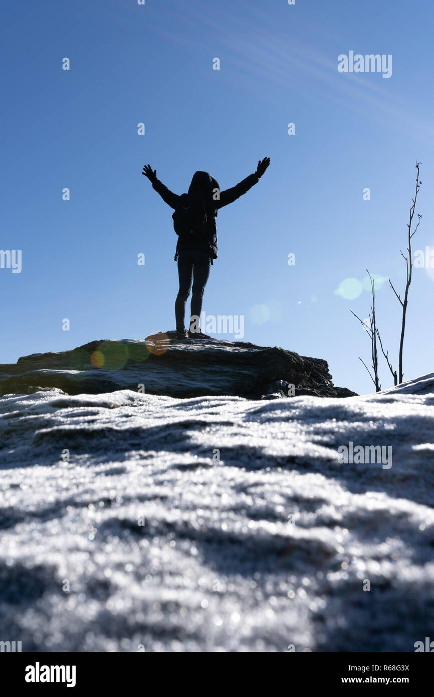 Cheering woman hiker bras ouverts au sommet de montagne avec de lourdes rétroéclairé et lens-flare crystalls glace au premier plan. Banque D'Images