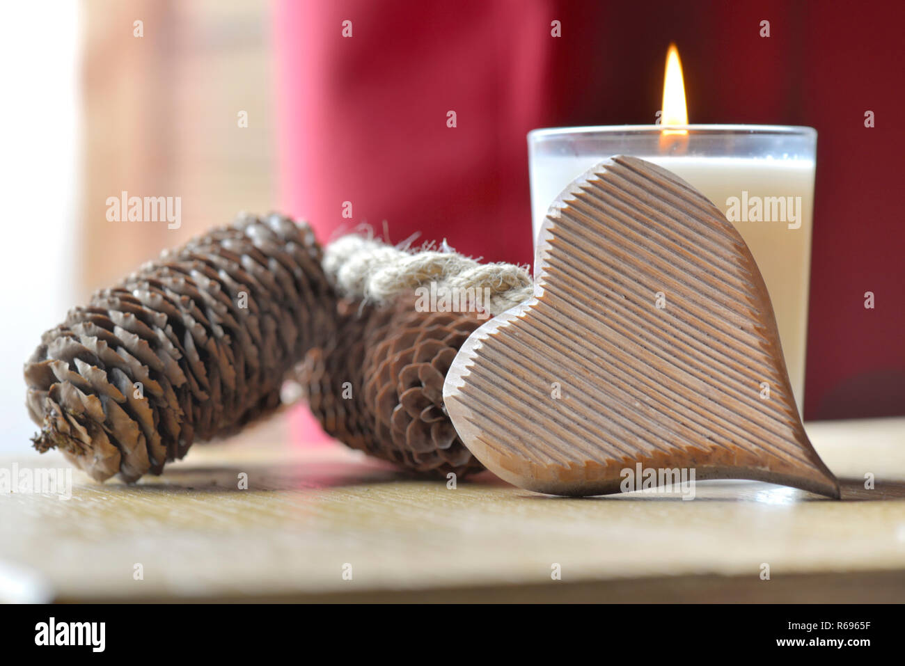 Coeur en bois contre une bougie avec des pommes de pin mis sur une table devant un rideau rouge Banque D'Images