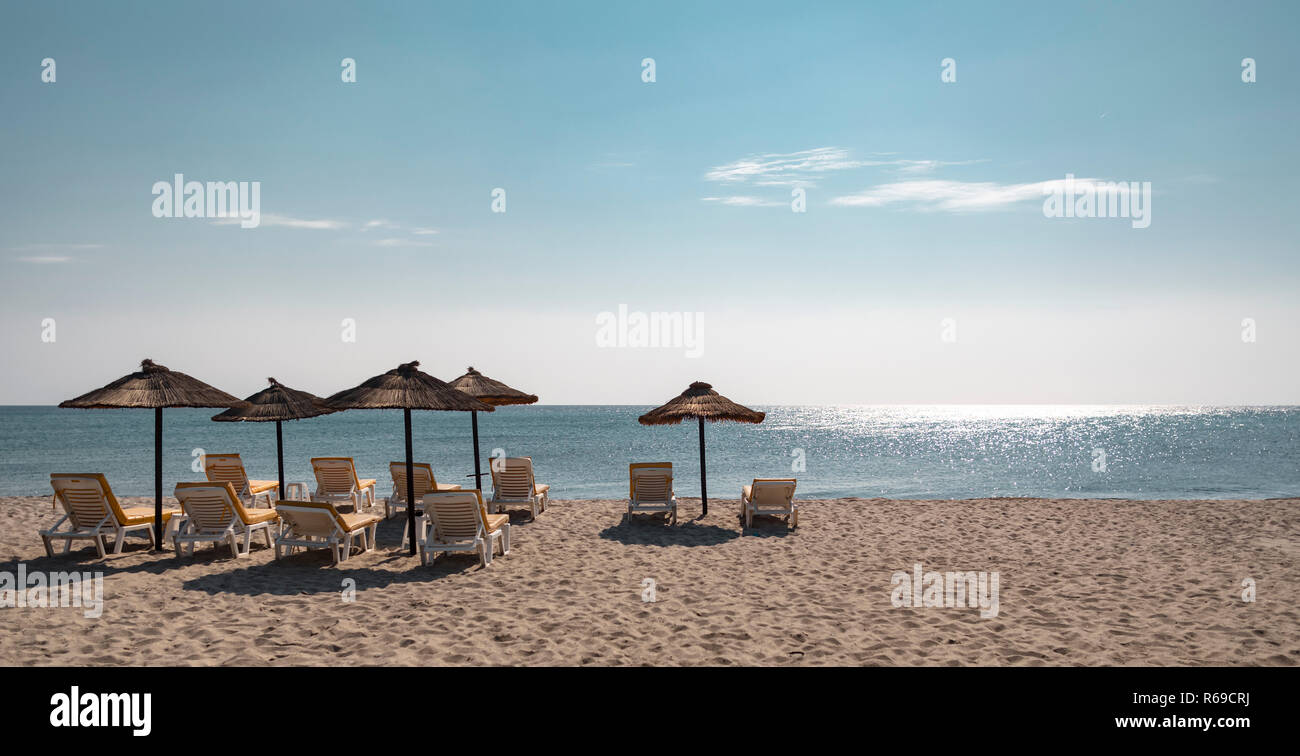Vue paysage de lounge fauteuils de relaxation et de paille a fait des parasols sur une plage de sable en face de la ligne d'horizon sur mer bleu turquoise. Banque D'Images