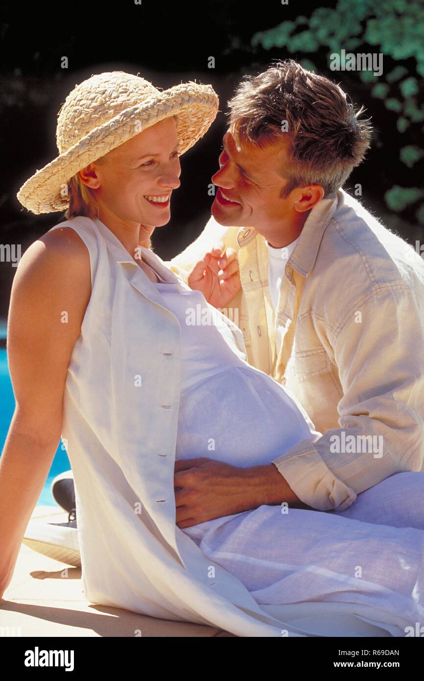 Piscine, Jeu, blonder Mann moechte seine schwangere weiss gekleidete Frau mit Strohhut kuessen Banque D'Images