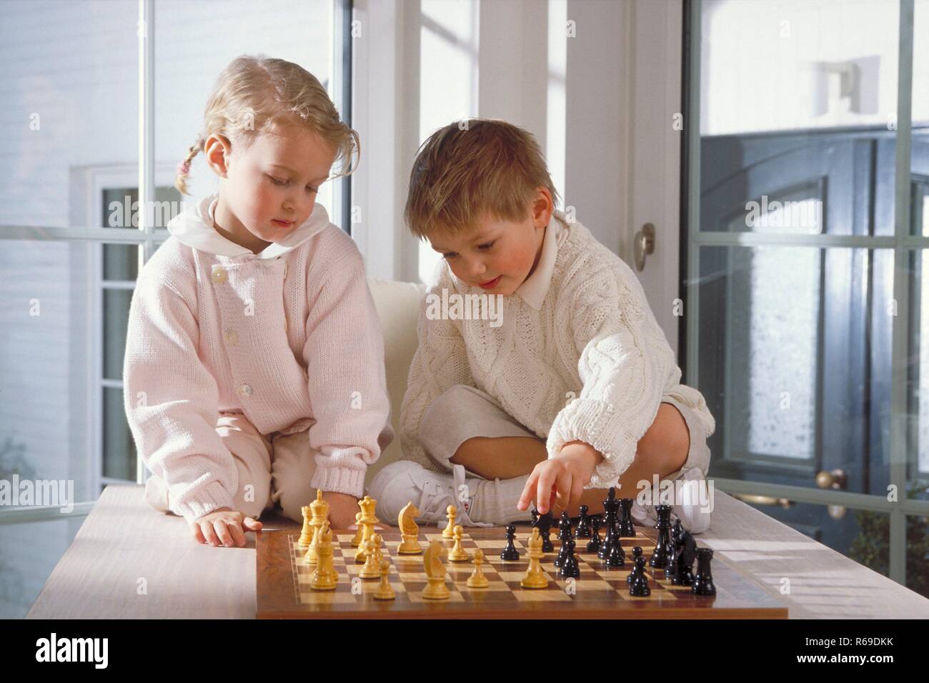 Portrait, Innenraum, Ganzfigur, blondes Maedchen und Junge, 4-5 Jahre alt, l'enfer beide gekleidet, sitzen auf dem Tisch und Spielen Schach Banque D'Images