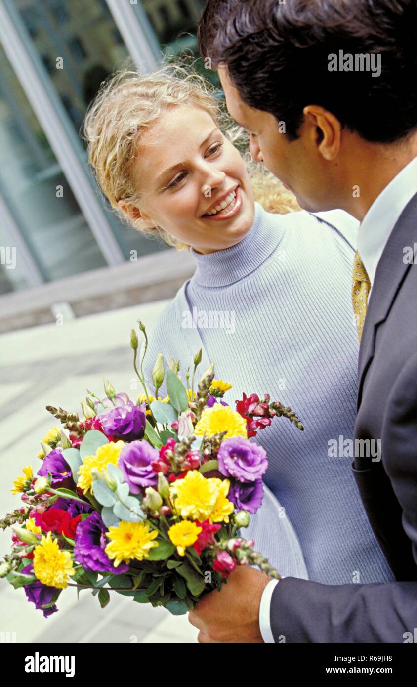 Portrait, Strassenszene, Halbfigur, junge Frau mit langem lockigen blondn Haar, bekleidet mit grauem Twinset, bekommt von ihrem Geliebten einem bunten Blumenstrauss ueberreicht Banque D'Images
