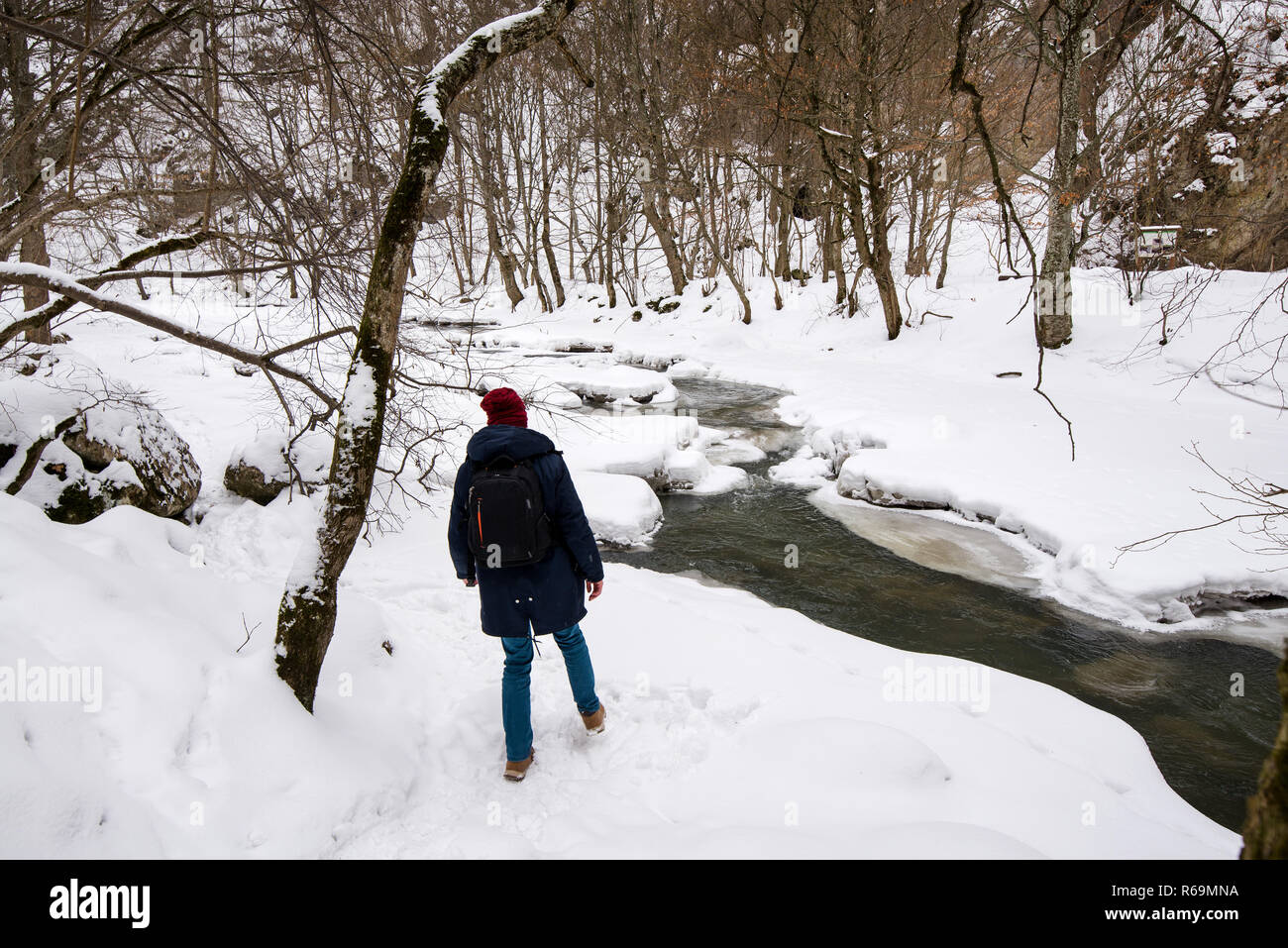 Homme randonnée dans la vallée de montagne à côté de rivière gelée recouverte de neige et de glace. Beau paysage d'hiver dans la forêt de montagne. Concept d'aventures et Banque D'Images