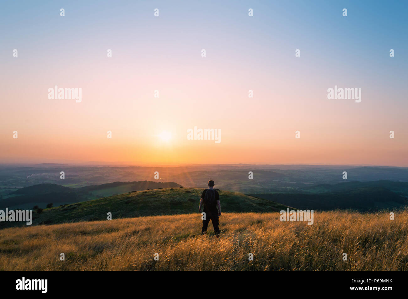 Randonneur sur une colline donnant sur le paysage anglais vers le coucher de soleil sur une soirée d'été. Banque D'Images