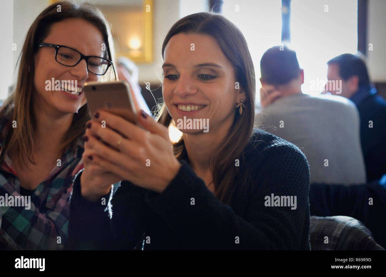 Les jeunes femmes à la recherche sur les smartphones et rire, Portrait, Café, Stuttgart, Bade-Wurtemberg, Allemagne Banque D'Images