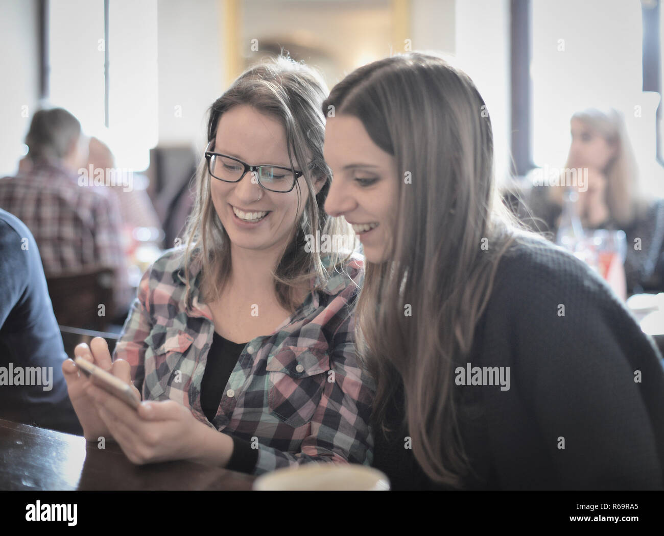 Les jeunes femmes à la recherche sur les smartphones et rire, Portrait, Café, Stuttgart, Bade-Wurtemberg, Allemagne Banque D'Images