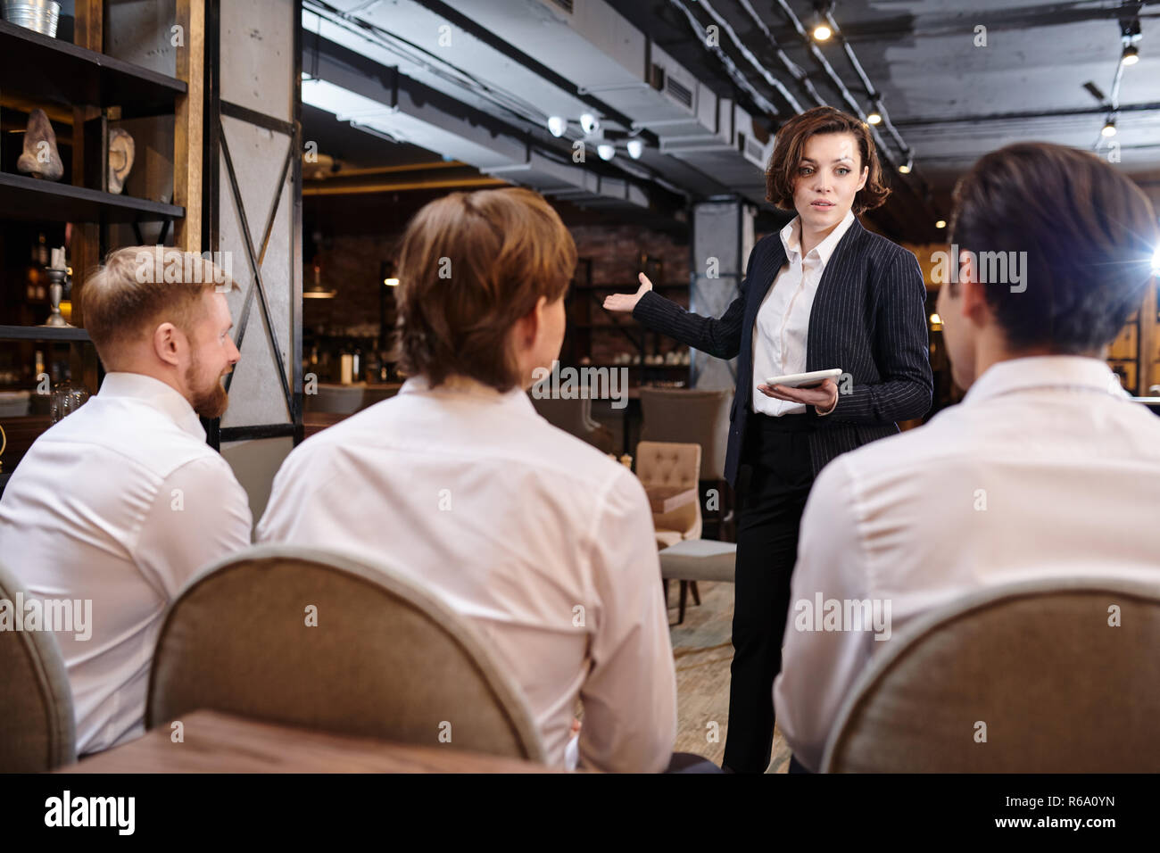 Jeune femme sérieuse confiance attrayant restaurant manager avec les cheveux courts debout devant des serveurs et à l'aide de tablet tout en expliquant les tâches à s Banque D'Images
