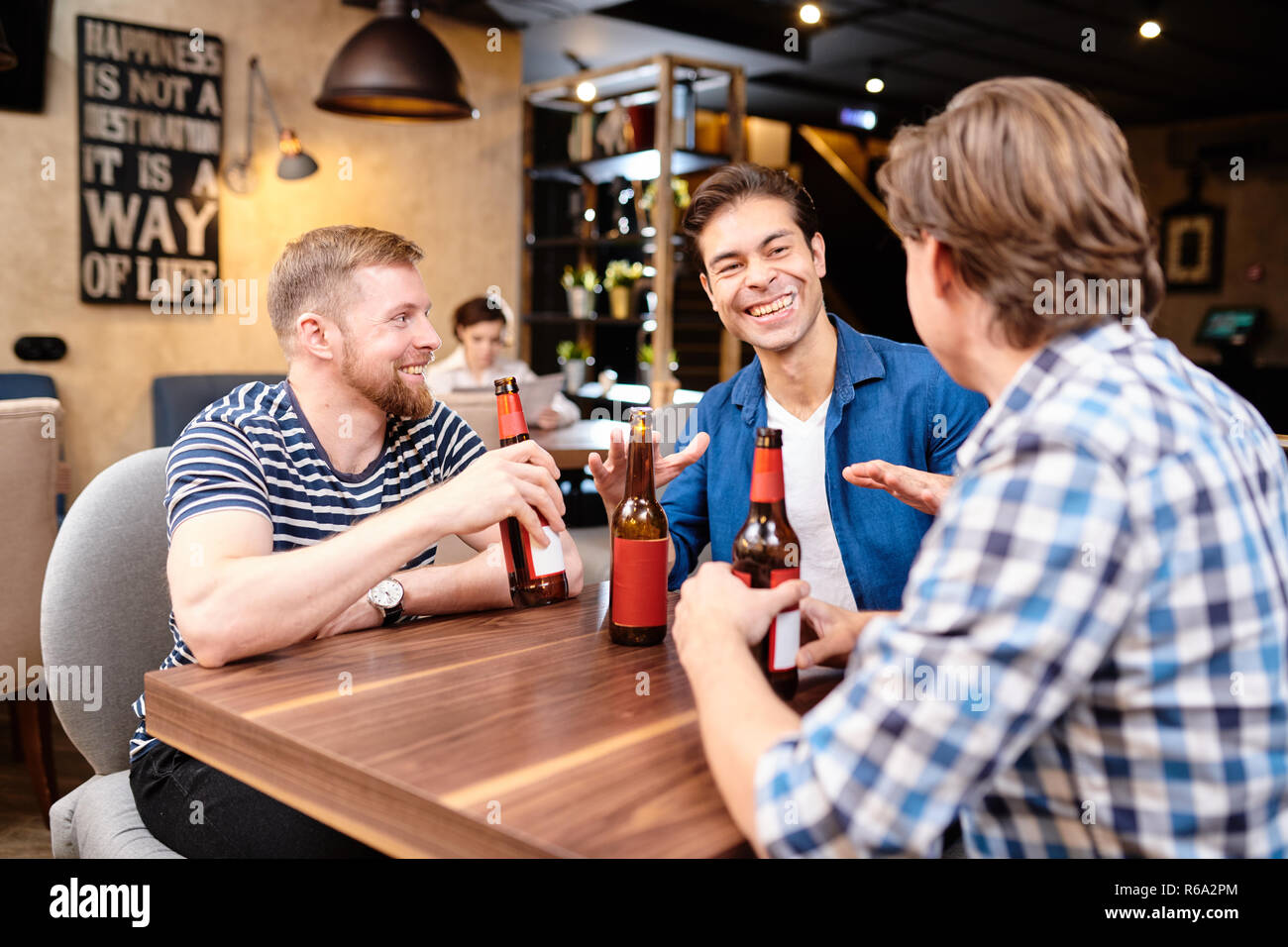 Jeune mâle extatique Jolly amis de vêtements, assis à table dans un bar et partager des histoires drôles alors que de boire une bière ensemble Banque D'Images