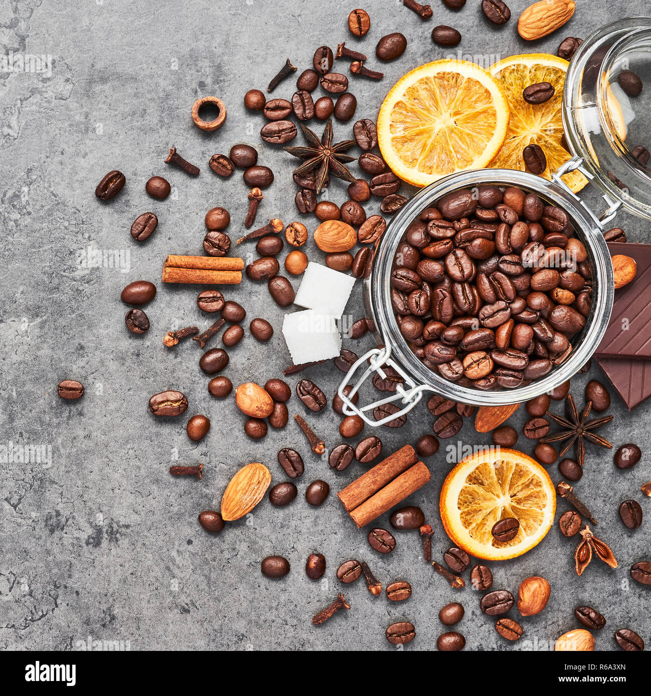 Café dans un bocal en verre avec des haricots, du chocolat, des oranges séchées, des bâtons de cannelle et anis sur fond de béton gris. Concept de café avec spi différents Banque D'Images