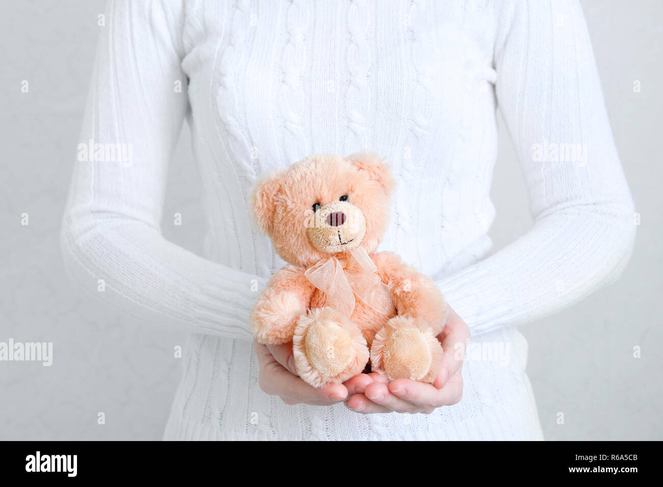 Jeune fille dans un chandail blanc tenant un ours en peluche. Arrière-plan blanc. Close-up. Banque D'Images