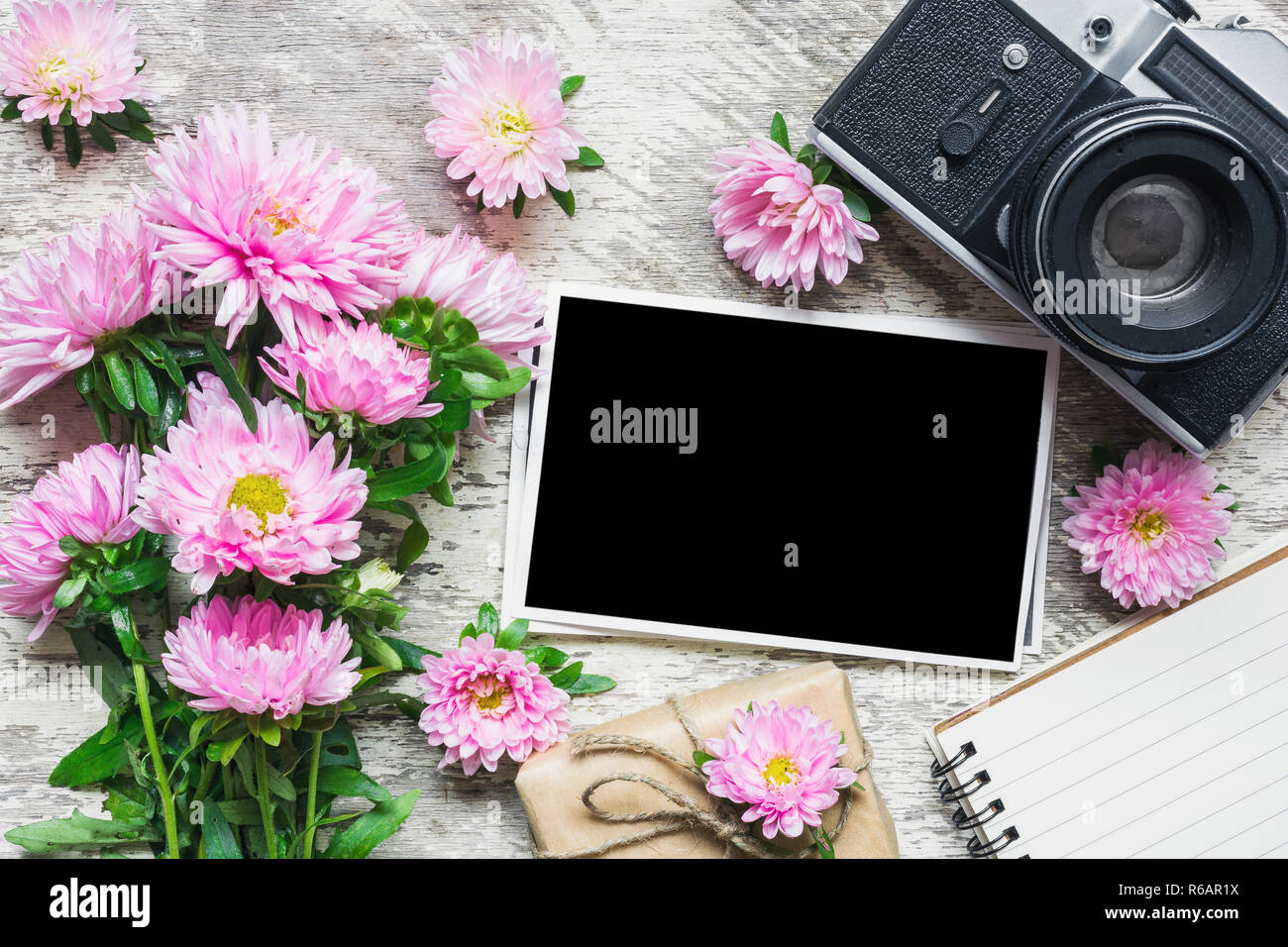 Cadre photo blanc retro vintage avec appareil photo et magnifique bouquet de fleurs aster rose, boîte cadeau et blank notepad. maison de vacances ou de mariage contexte. mo Banque D'Images