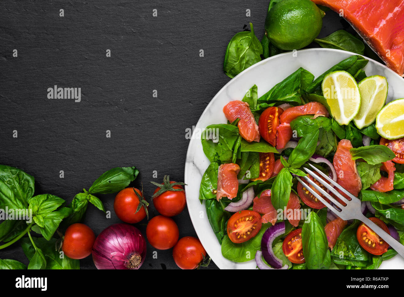 Salade fraîche au saumon, épinards, tomates cerises, l'oignon rouge et le basilic dans la plaque de marbre avec une fourchette sur fond d'ardoise noire. Une alimentation saine à concept. Banque D'Images