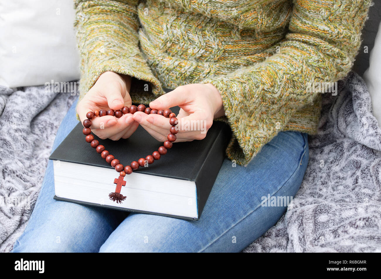 Une fille dans un chandail vert tient une bible et un chapelet en bois d'une croix. Banque D'Images