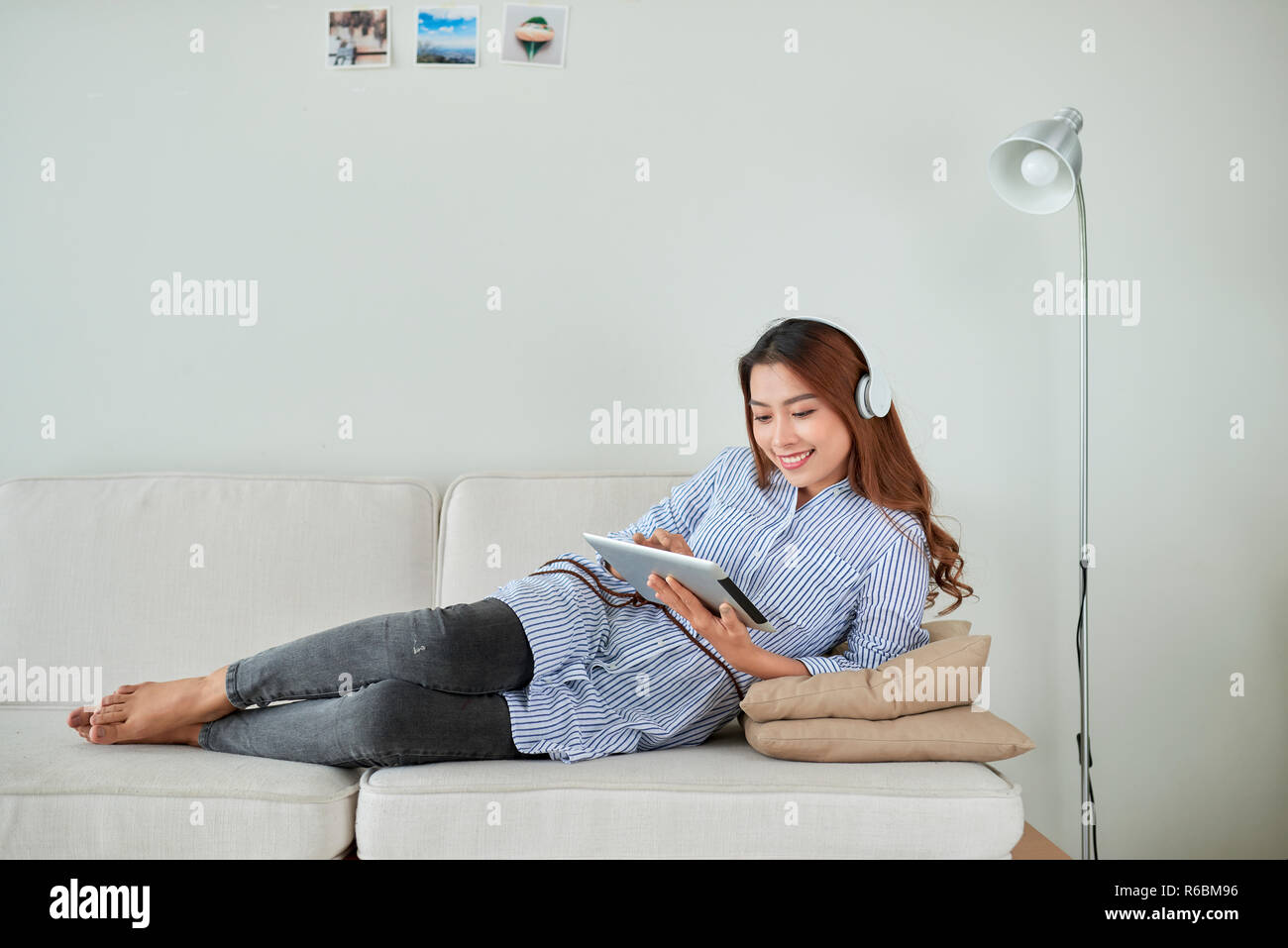 Jolie jeune femme porter des écouteurs assis sur un canapé et usinging sur tablette. Banque D'Images