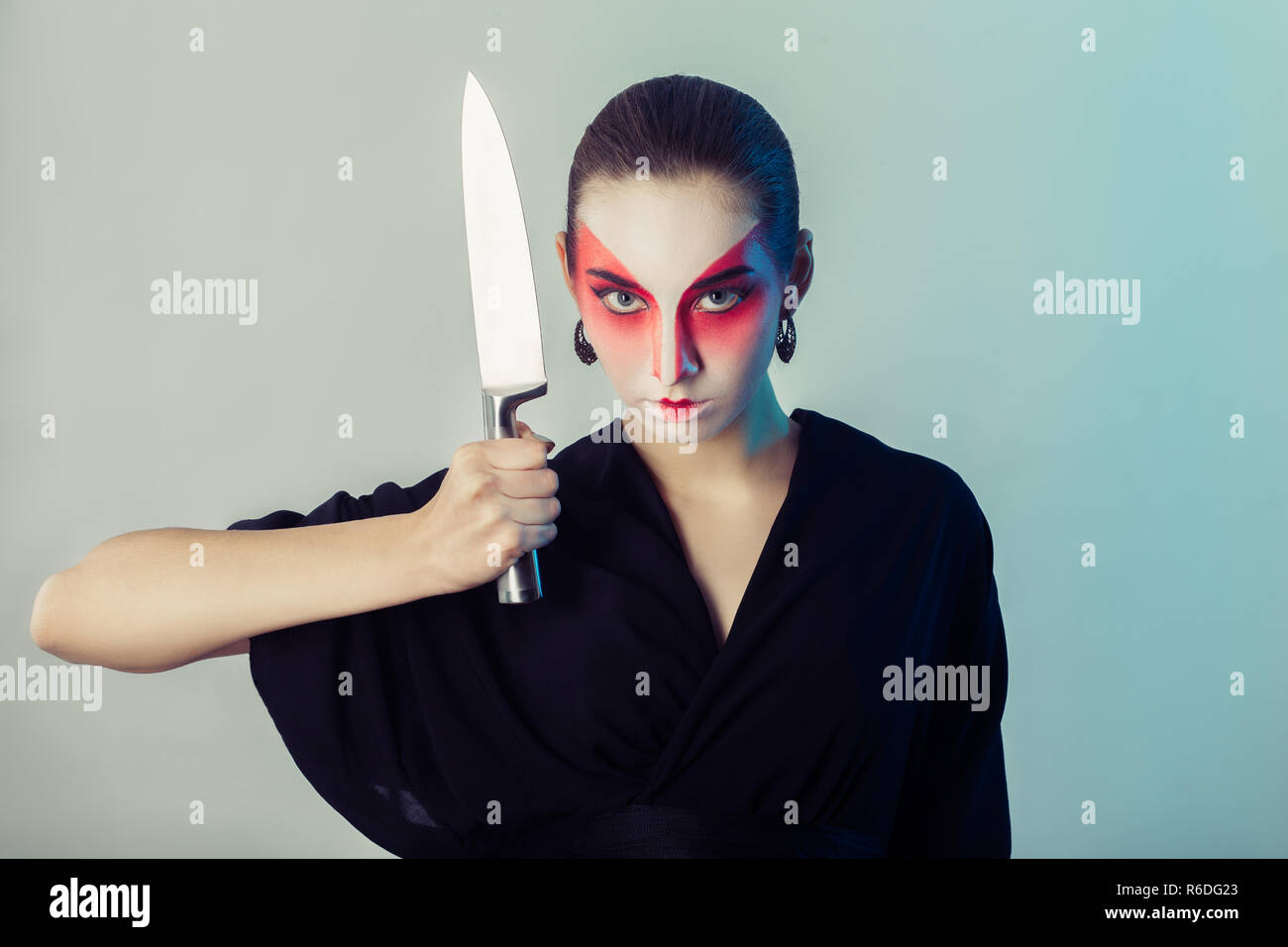Femme sérieuse, professionnelle, maquillage geisha en kimono noir avec grand couteau de cuisine, looking at camera Banque D'Images