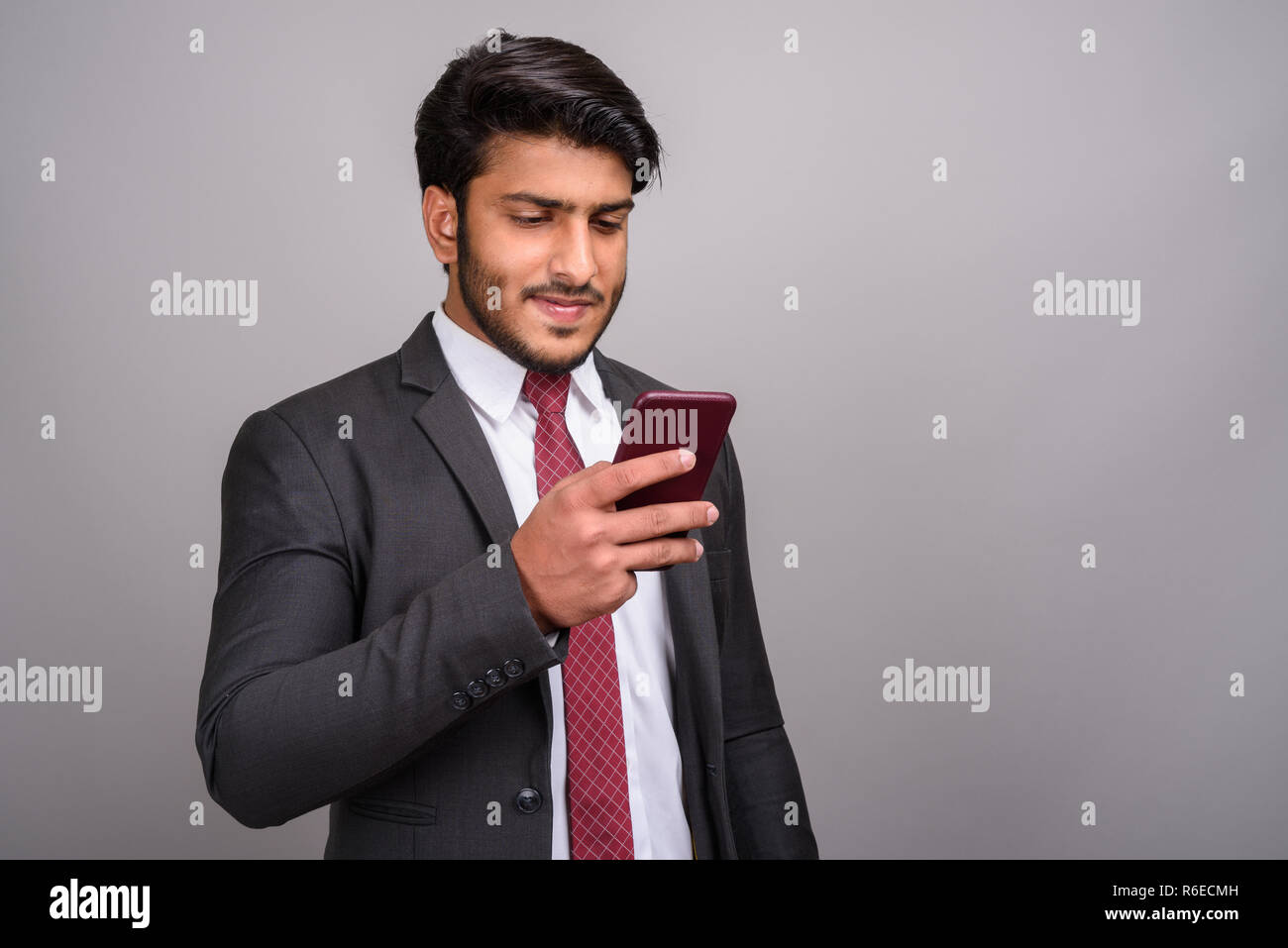 Portrait of Indian businessman using mobile phone contre l'arrière-plan gris Banque D'Images