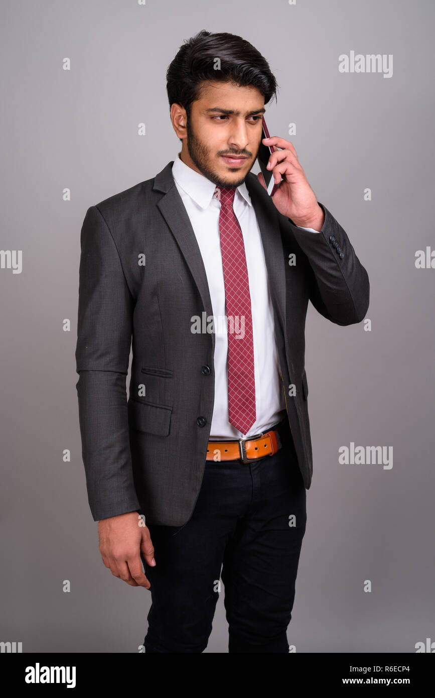 Portrait of Indian businessman using mobile phone contre l'arrière-plan gris Banque D'Images