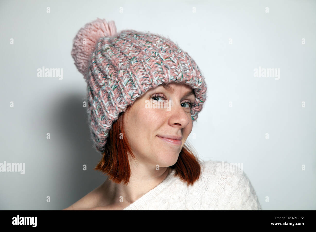 Portrait isolé belle jeune fille rousse yeux vert pull blanc et rose avec Chapeau tricoté pompon habillé latéralement sur fond blanc dans studi Banque D'Images