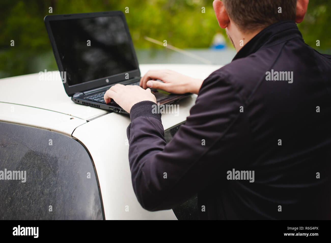 Homme avec un ordinateur portable en stationnement dans une cour près de voiture est de faire manipulations avec système cybernétique, concept Banque D'Images