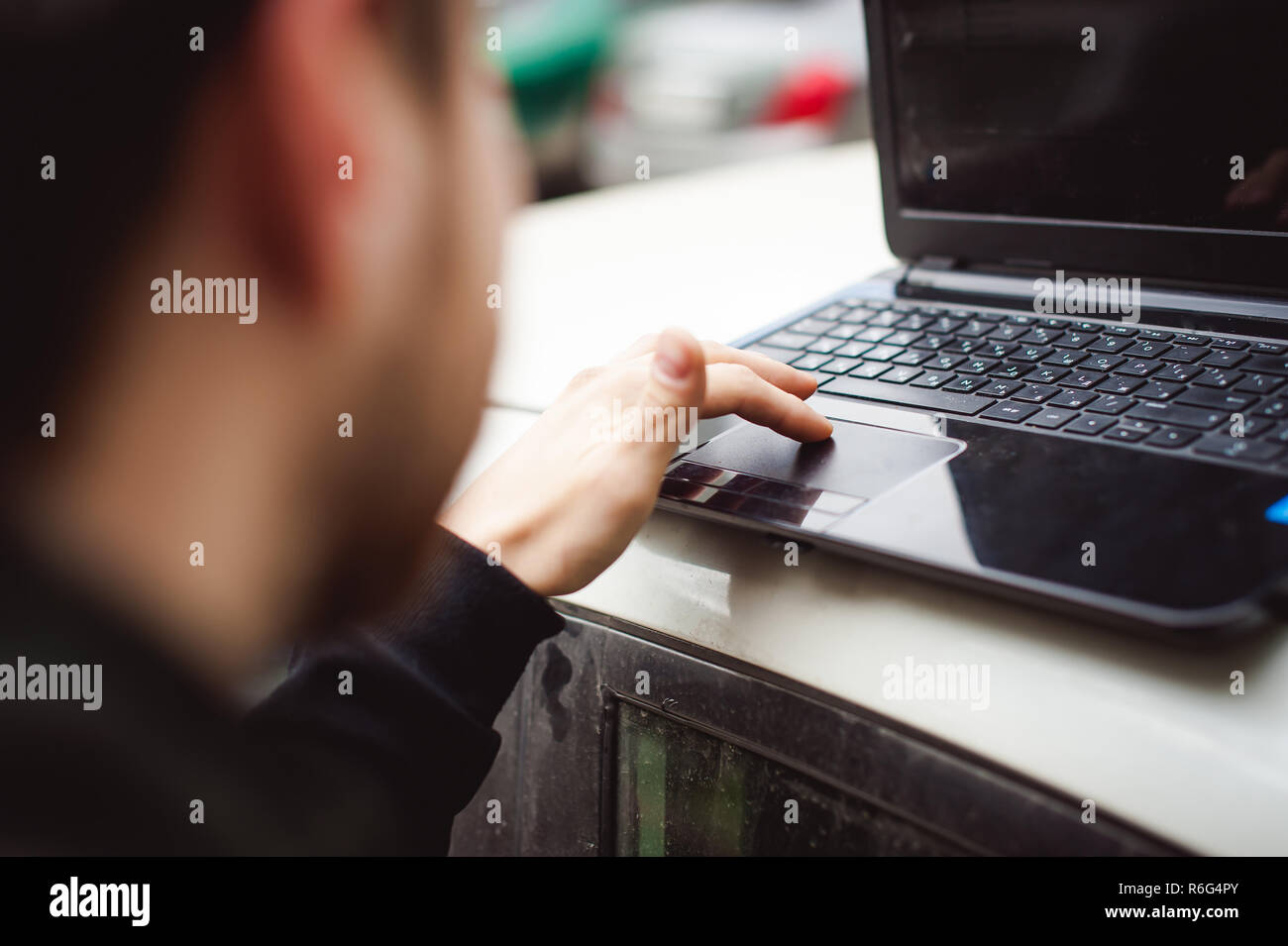 Homme avec un ordinateur portable en stationnement dans une cour près de voiture est de faire manipulations avec système cybernétique, concept Banque D'Images