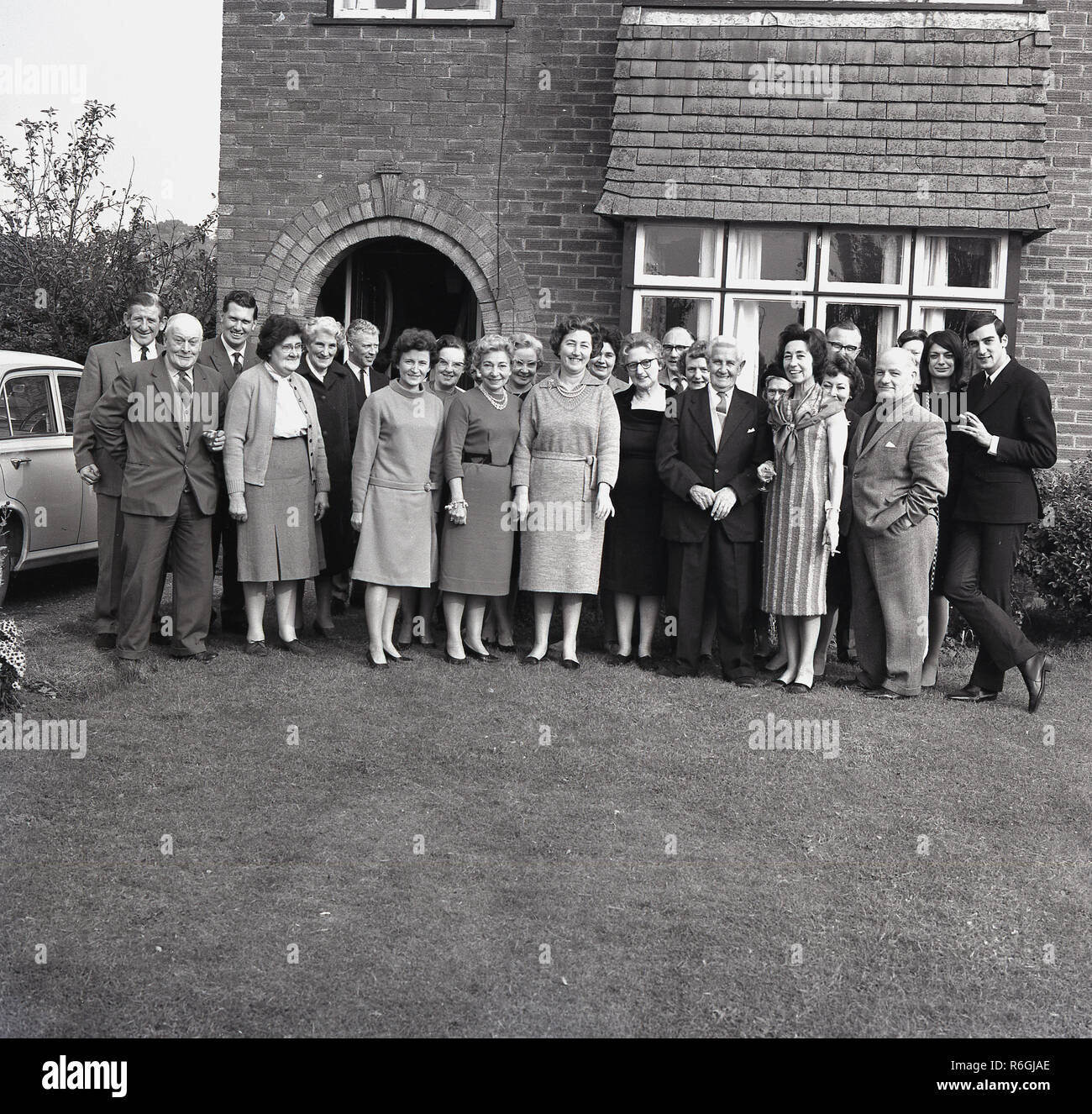 Années 1960, historiques, une famille se rassemblent à l'extérieur d'une maison de banlieue de poser pour une photo de groupe pour célébrer un anniversaire de mariage du couple, England, UK. Un mariage d'or célèbre 50 années de vie de couple, un accomplissement d'un grand amour et d'engagement. Banque D'Images