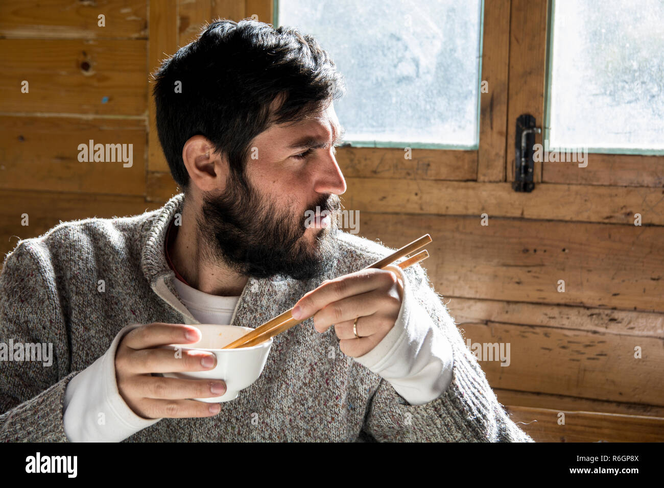 Portrait d'un homme barbu coin et tenait un bol et baguettes dans une cabane en bois, Yading, Chine. Banque D'Images