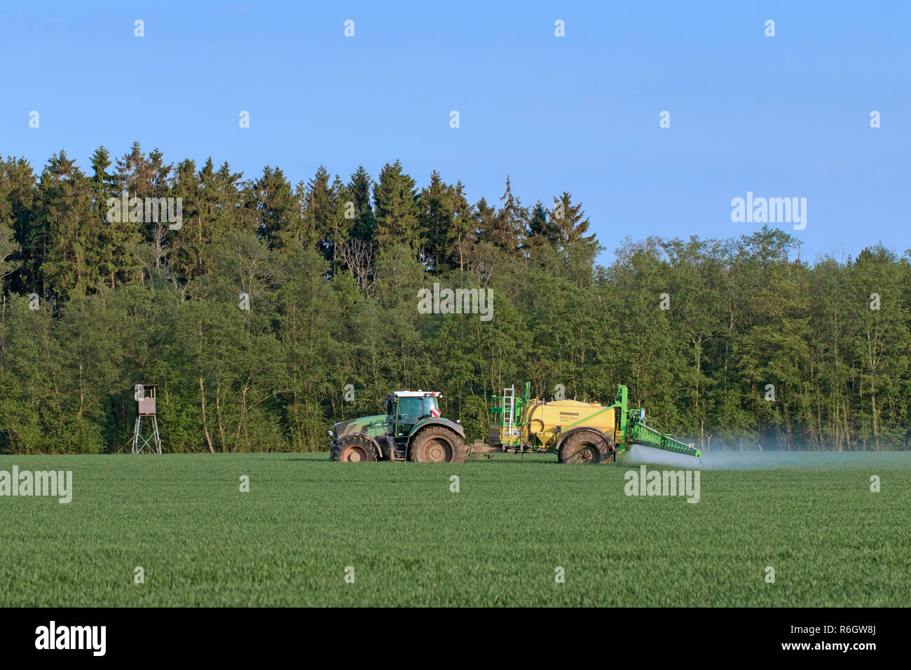 Agriculteur dans le tracteur l'épandage d'herbicides / insecticides / pesticides sur terrain avec pulvérisateur traîné au printemps Banque D'Images
