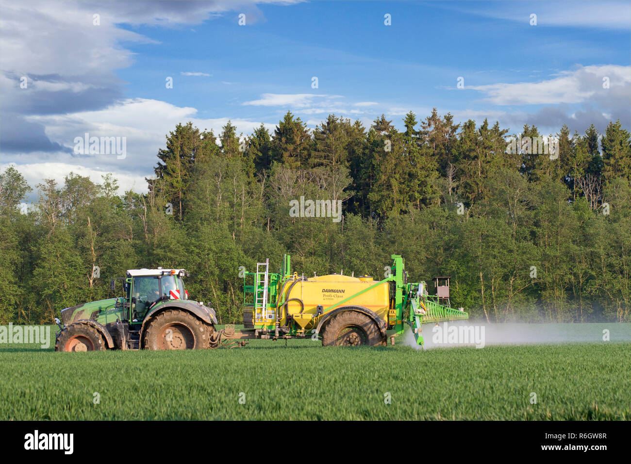 Agriculteur dans le tracteur l'épandage d'herbicides / insecticides / pesticides sur terrain avec pulvérisateur traîné au printemps Banque D'Images