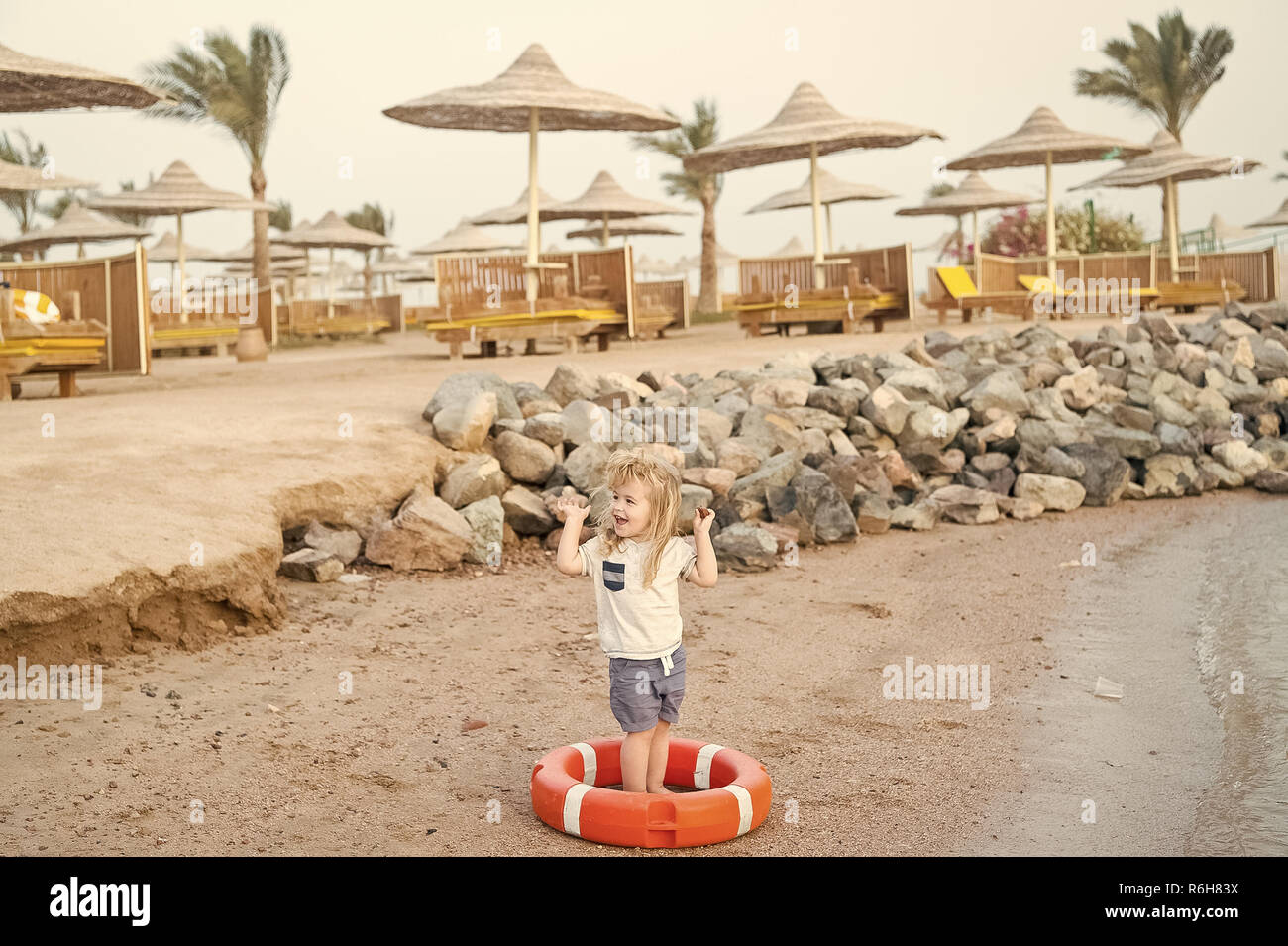 Petit Garcon De Bebe Ou Enfant Mignon Visage Heureux Et Avec Des Cheveux Blonds En Shirt Short Et Pieds Nus Jouant Avec La Ceinture Rouge Ou Bouee A Plage De Sable Avec
