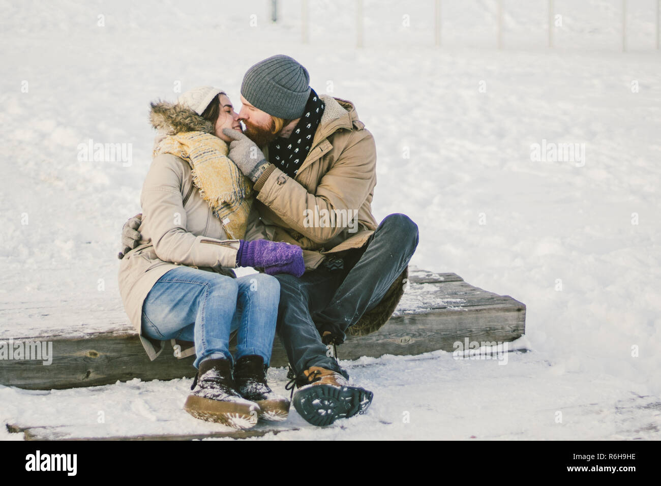 Couple aimant les jeunes un homme avec une barbe et une femme de race blanche sont assis sur un escalier en bois en hiver sur la neige La Saint-Valentin un Banque D'Images