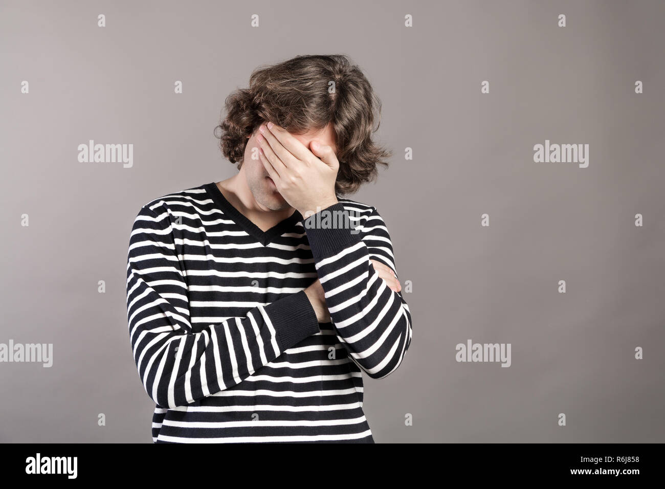 Portrait de l'homme perturbé couvrant son visage avec la main isolé sur fond gris. Facepalm de l'expression du visage. Déçu jeune homme hirsute rasée couvrant son visage avec sa main. Les émotions négatives. Banque D'Images