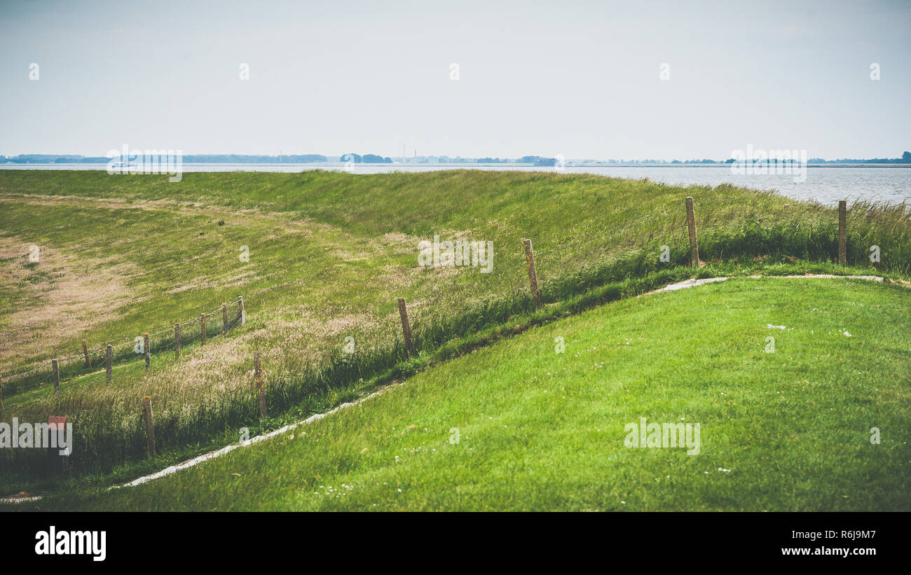 Vue panoramique d'un polder en Hollande un paysage plat typiquement néerlandais avec de l'eau, une digue et quelques moulins à vent à l'horizon. Banque D'Images