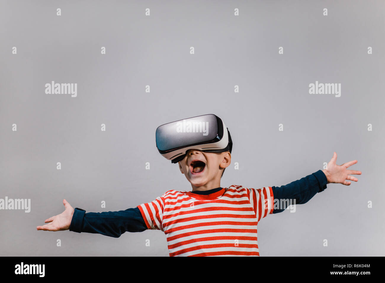 Portrait of happy child wearing casque de réalité virtuelle contre un arrière-plan gris. Heureux gamin avec mains propagation s'amusant avec lunettes VR. Banque D'Images