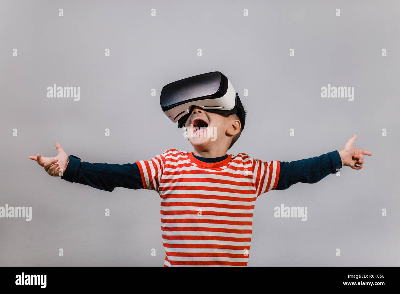 Portrait of happy child wearing casque de réalité virtuelle contre un arrière-plan gris. Heureux gamin avec mains propagation s'amusant avec lunettes VR. Banque D'Images