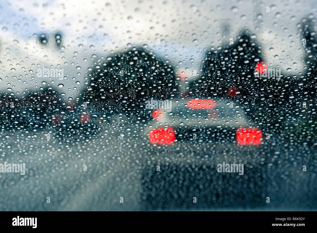 Gouttes de pluie sur le pare-brise un jour de pluie ; troubles de voiture s'est arrêtée à un feu de circulation à l'arrière-plan ; Californie Banque D'Images