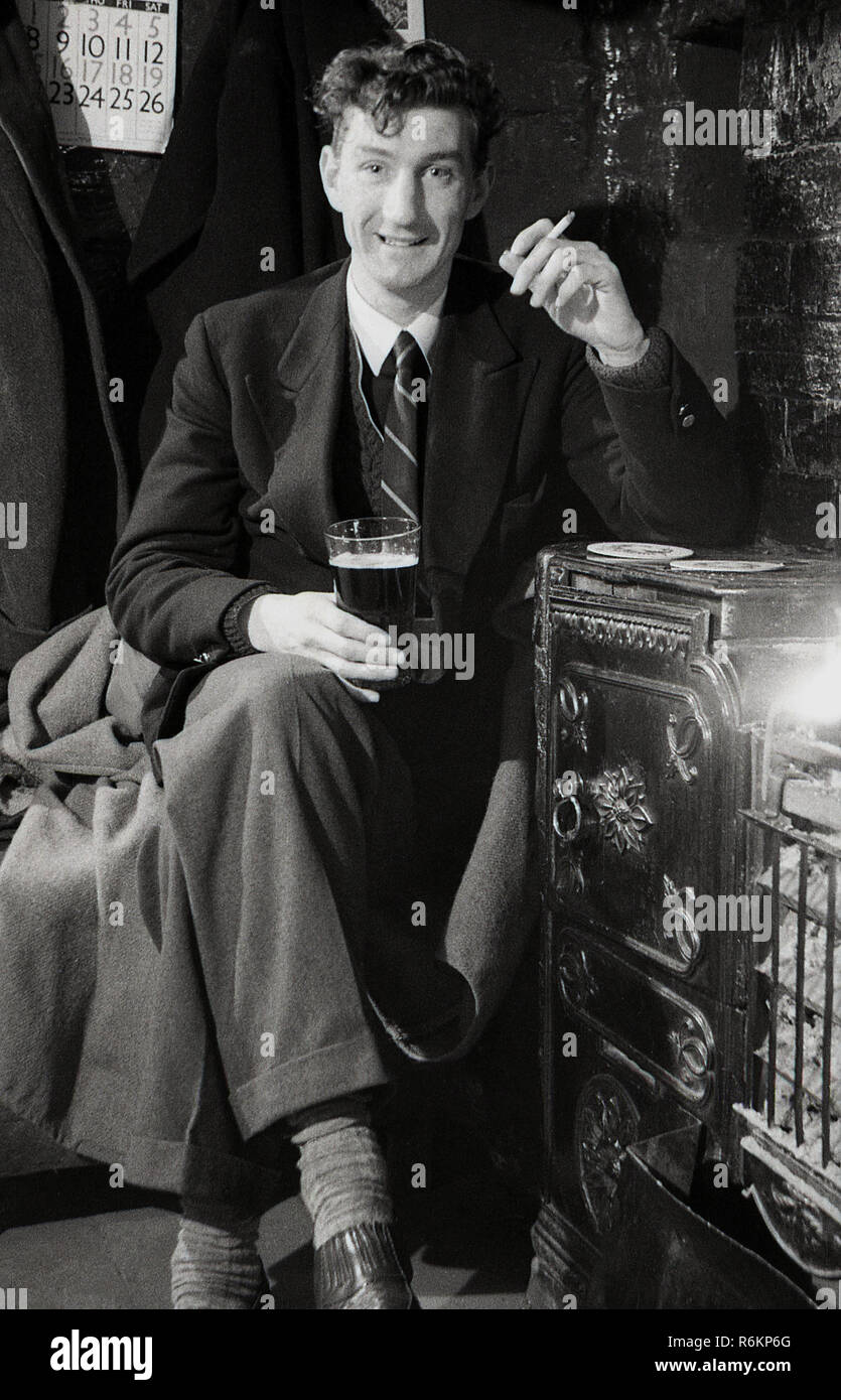 1940, historique, un jeune homme, dans la vingtaine, portant un veston et  une cravate, dans un pub assis par un incendie ayant une pinte de bière et  une cigarette Photo Stock - Alamy