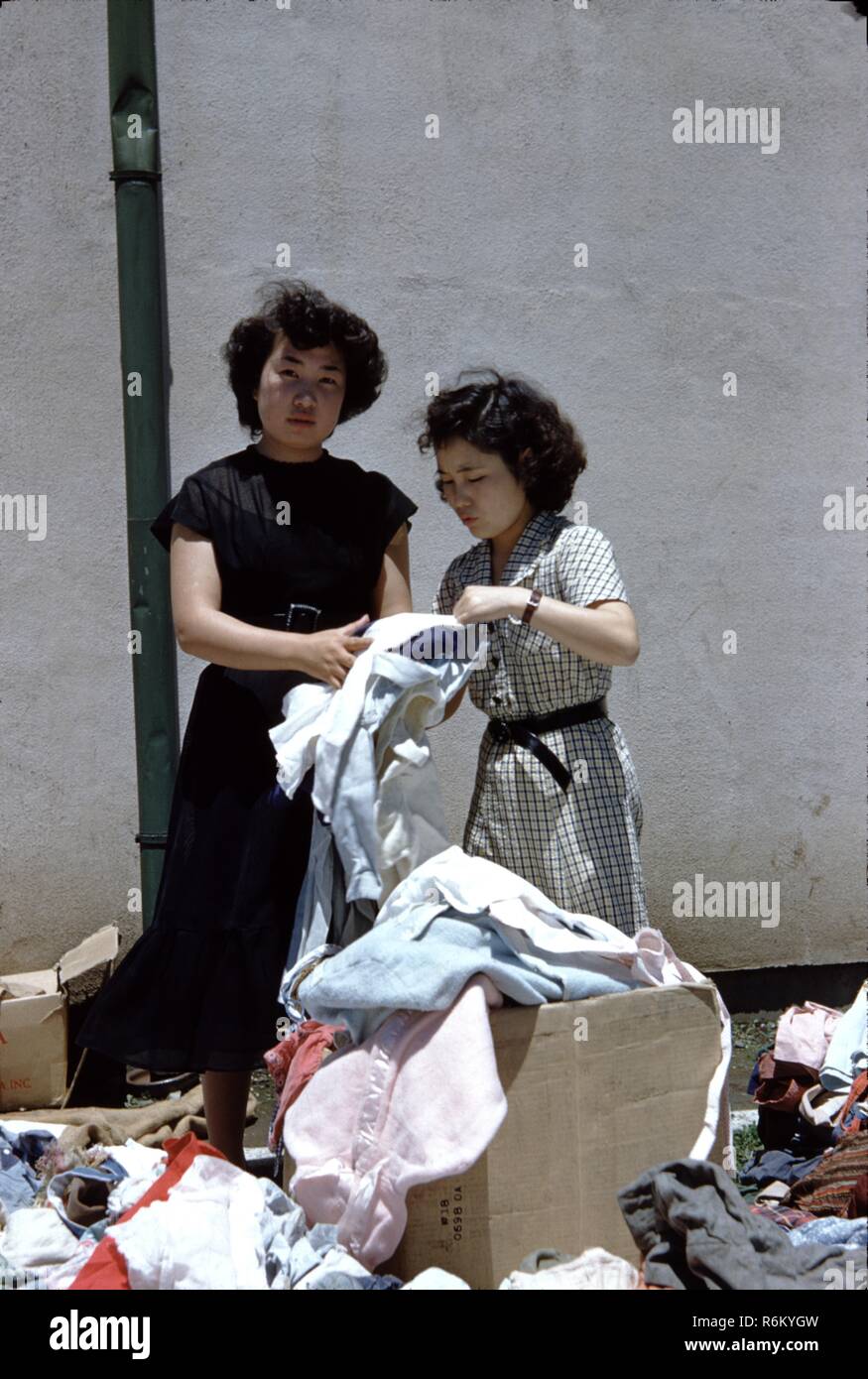 Deux japonaises le tri d'une boîte de vêtements colorés, peut-être une partie d'un don de bienfaisance, Japon, 1955. () Banque D'Images