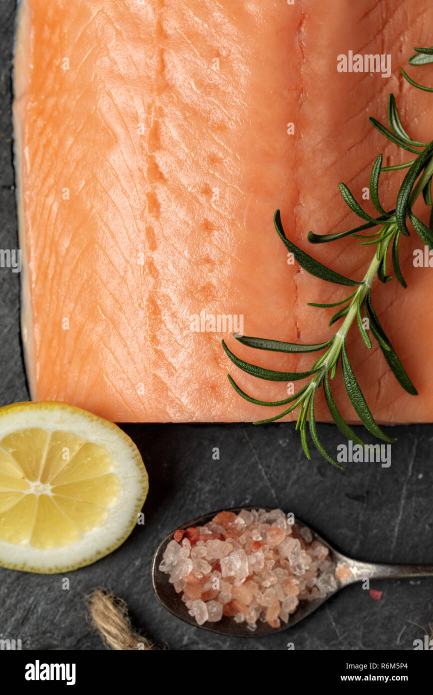 Filet de saumon cru sur la plaque en ardoise noire et ingrédients pour  faire gravlax. Le sel, le sucre, le citron et le romarin dans  l'arrière-plan de traitement à sec la marinade,