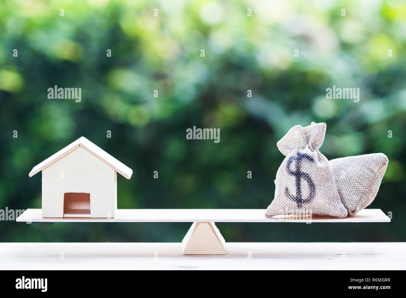 Maison de prêt, les prêts hypothécaires, de la dette, l'épargne de l'argent pour l'achat d'une maison concept : un équilibre entre un sac d'argent et petite résidence, maison modèle sur le tableau contre green natu Banque D'Images